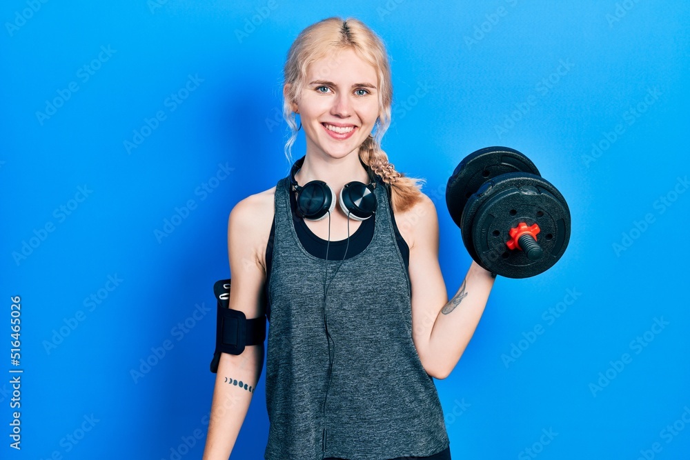 Beautiful caucasian sports woman with blond hair wearing sportswear using dumbbells looking positive and happy standing and smiling with a confident smile showing teeth Beautiful caucasian sports woman with blond hair wearing sportswear using dumbbells looking positive and happy standing and smiling with a confident smile showing teeth