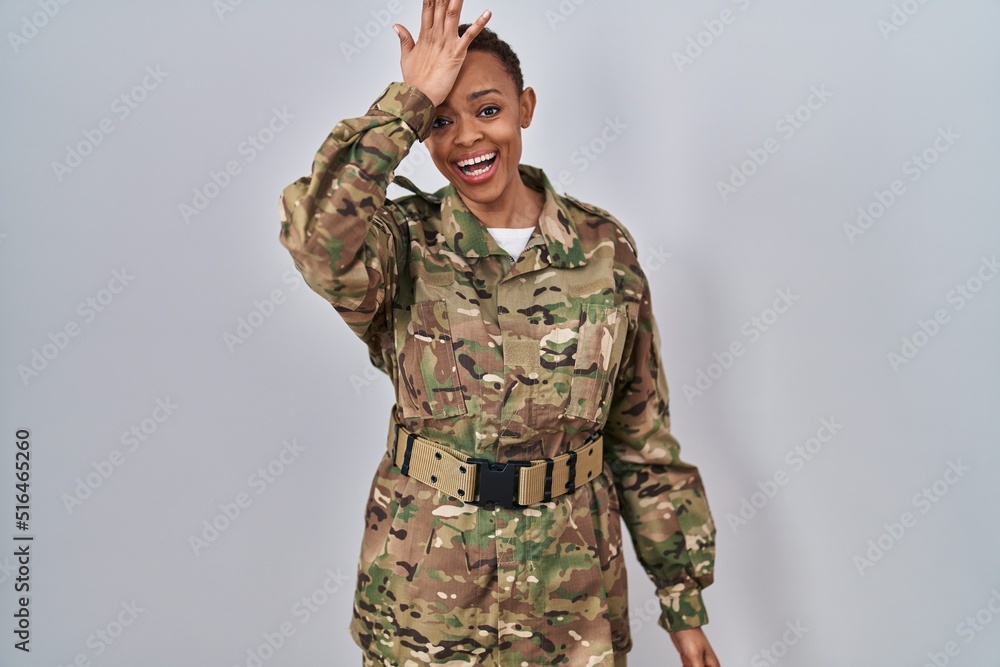 Beautiful african american woman wearing camouflage army uniform surprised with hand on head for mistake, remember error. forgot, bad memory concept. Beautiful african american woman wearing camouflage army uniform surprised with hand on head for mistake, remember error. forgot, bad memory concept.