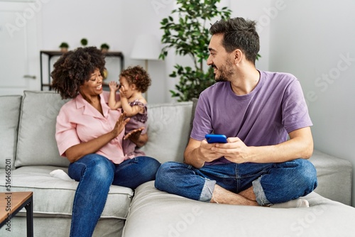 Couple and daughter using smartphone sitting on sofa at home