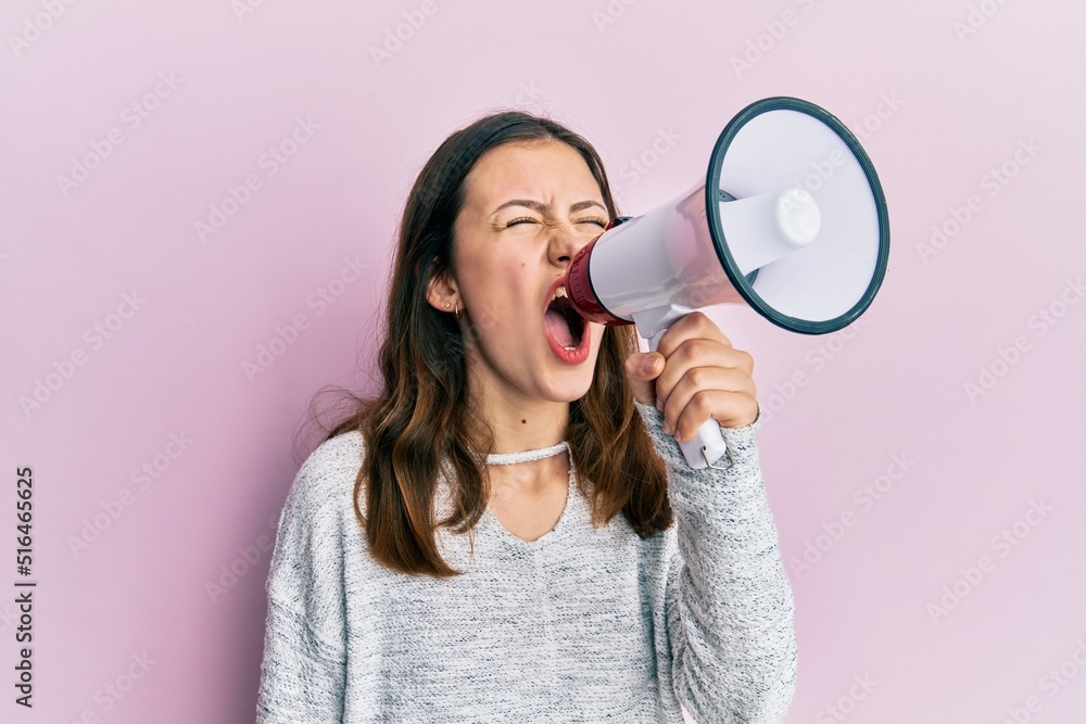 Young brunette woman shouting and screaming through megaphone over pink isolated background Young brunette woman shouting and screaming through megaphone over pink isolated background