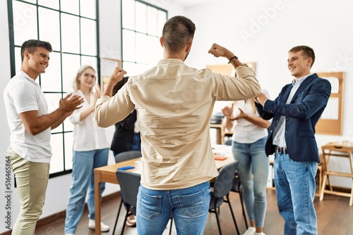 Group of young business workers smiling and clapping. Young businessman doing strong gesture with arms on back view at the office.