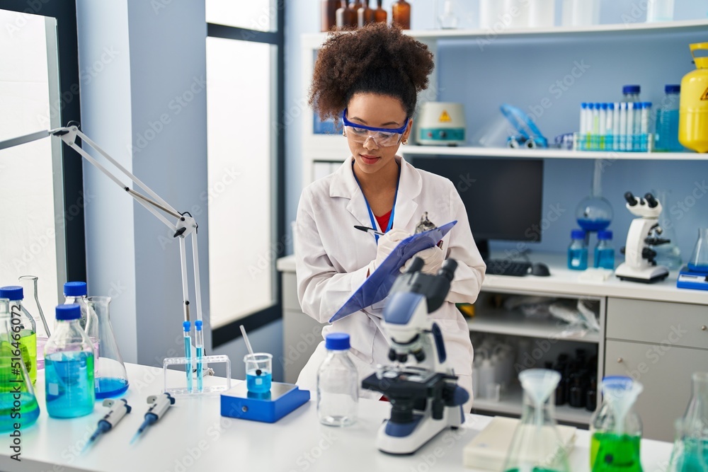 Young african american woman wearing scientist uniform writing on