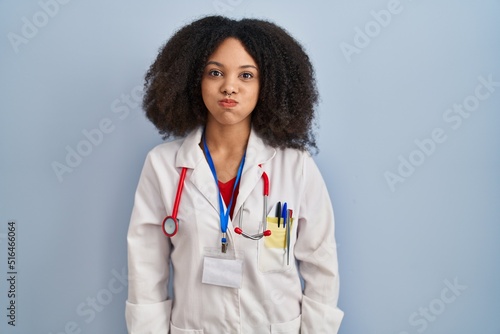 Young african american woman wearing doctor uniform and stethoscope puffing cheeks with funny face. mouth inflated with air, crazy expression.