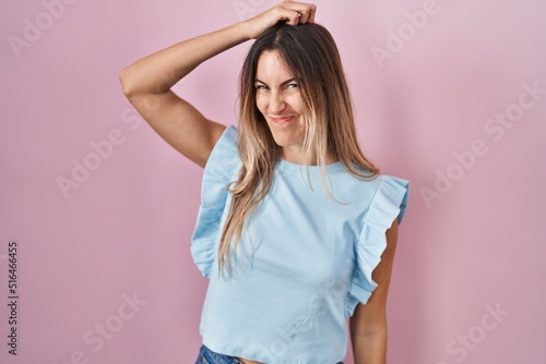 Young hispanic woman standing over pink background confuse and wonder about question. uncertain with doubt, thinking with hand on head. pensive concept.