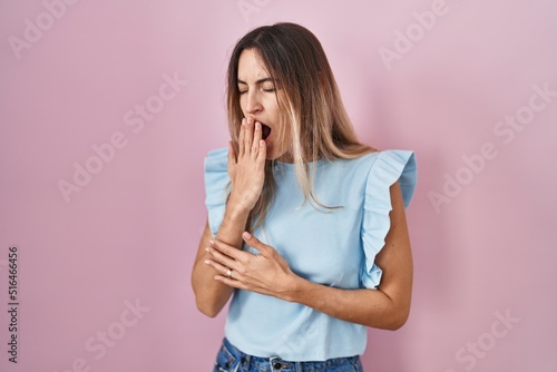 Young hispanic woman standing over pink background bored yawning tired covering mouth with hand. restless and sleepiness.