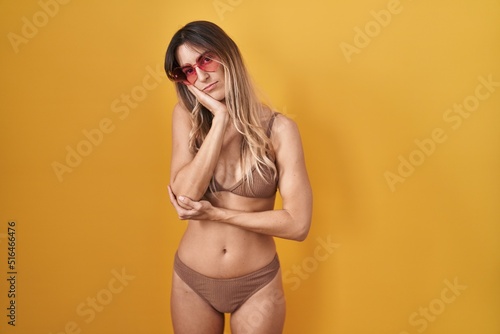 Young hispanic woman wearing bikini over yellow background thinking looking tired and bored with depression problems with crossed arms.