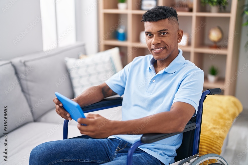 Young latin man using touchpad sitting on wheelchair at home Young latin man using touchpad sitting on wheelchair at home