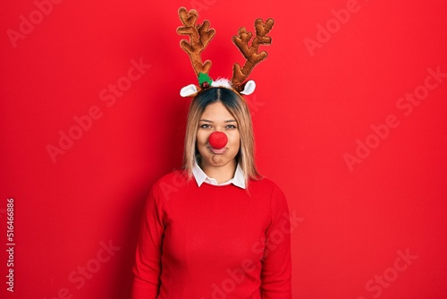 Fototapeta Naklejka Na Ścianę i Meble -  Beautiful hispanic woman wearing deer christmas hat and red nose puffing cheeks with funny face. mouth inflated with air, crazy expression.