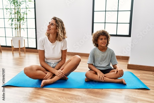 Young woman and son sitting on training mat at the gym looking away to side with smile on face  natural expression. laughing confident.