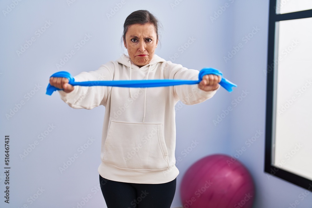 Middle age hispanic woman training arm resistance with elastic arm bands skeptic and nervous, frowning upset because of problem. negative person. Middle age hispanic woman training arm resistance with elastic arm bands skeptic and nervous, frowning upset because of problem. negative person.