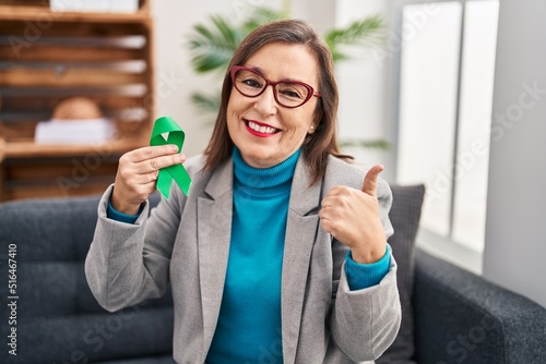 Middle age hispanic woman holding support green ribbon smiling happy and positive  thumb up doing excellent and approval sign