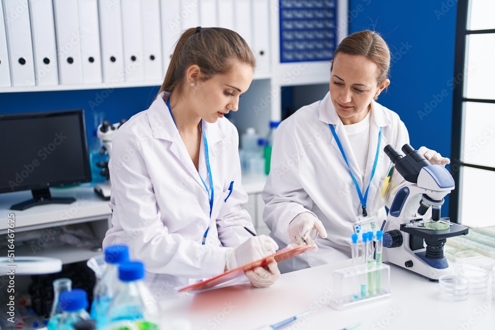 Two women scientists using microscope and write on document at laboratory Two women scientists using microscope and write on document at laboratory