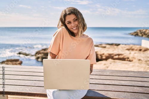 Young hispanic woman talking on the smartphone using laptop at seaside