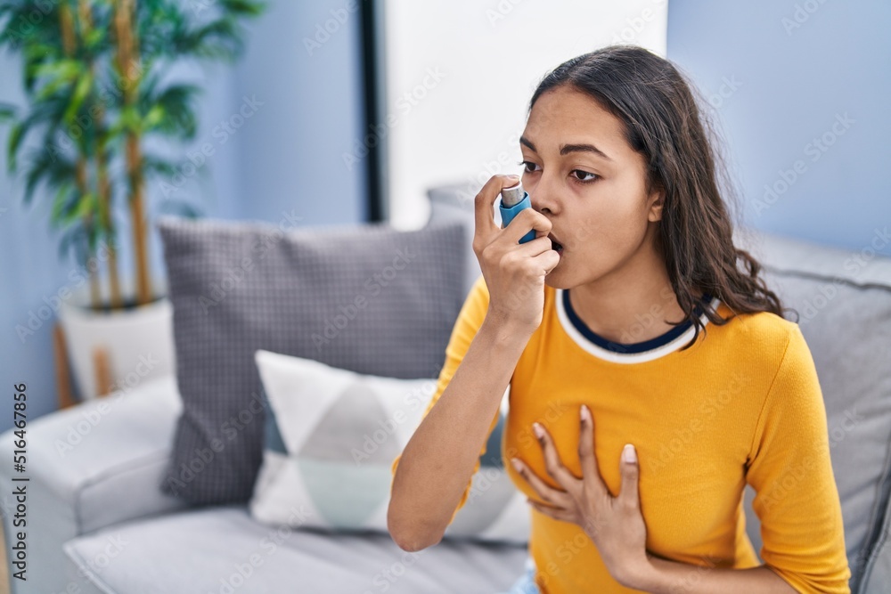 Young african american woman using inhaler sitting on sofa at home Young african american woman using inhaler sitting on sofa at home
