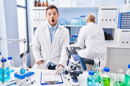 Hispanic man and woman working at scientist laboratory scared and amazed with open mouth for surprise  disbelief face