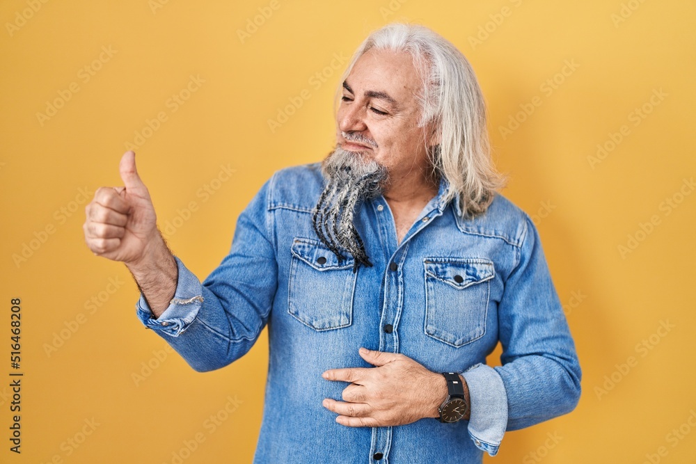 Obraz premium Middle age man with grey hair standing over yellow background looking proud, smiling doing thumbs up gesture to the side