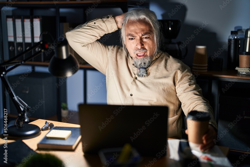 Middle age man with grey hair working at the office at night crazy and scared with hands on head, afraid and surprised of shock with open mouth Middle age man with grey hair working at the office at night crazy and scared with hands on head, afraid and surprised of shock with open mouth