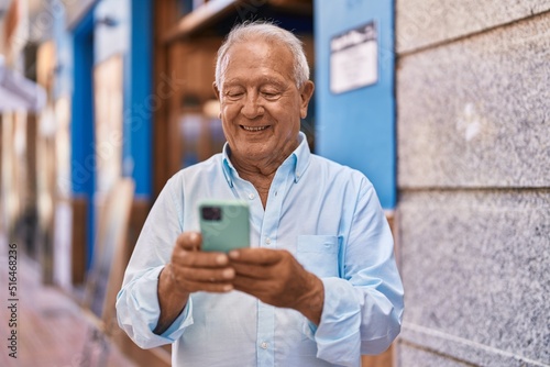 Senior grey-haired man smiling confident using smartphone at street