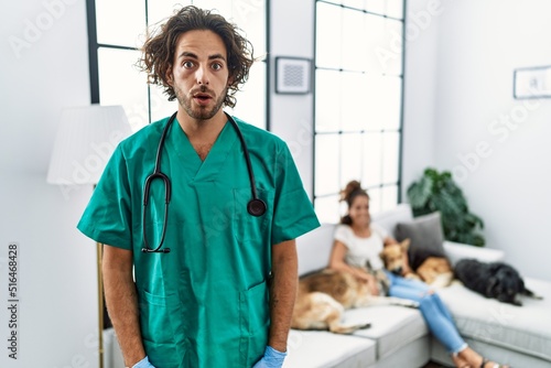 Photography Young veterinarian man checking dogs at home scared and amazed with open mouth f