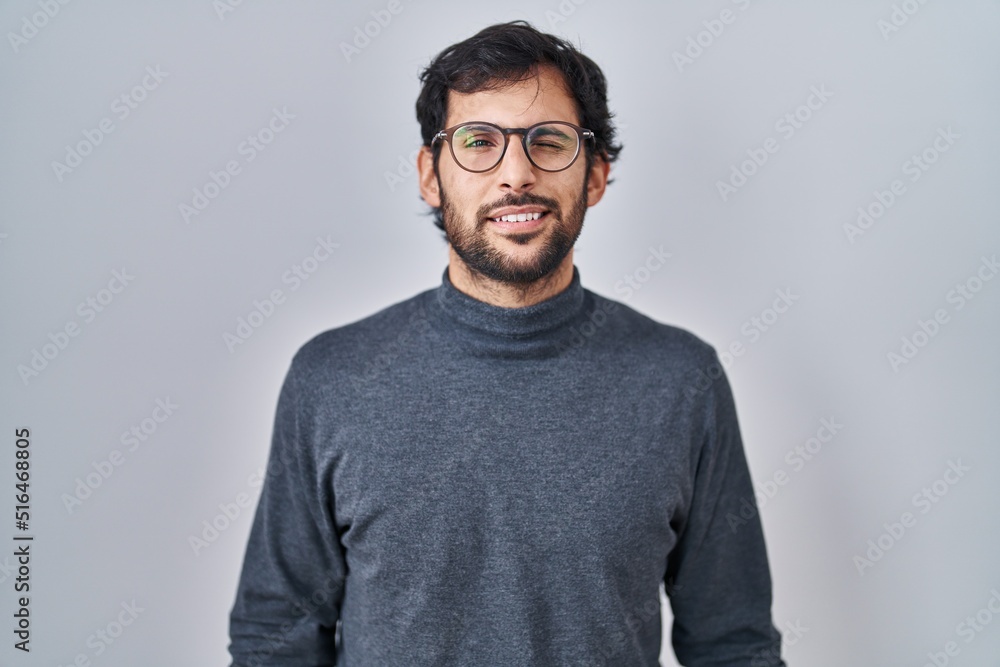 Handsome latin man standing over isolated background winking looking at the camera with sexy expression, cheerful and happy face. Handsome latin man standing over isolated background winking looking at the camera with sexy expression, cheerful and happy face.