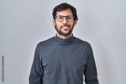 Handsome latin man standing over isolated background winking looking at the camera with sexy expression, cheerful and happy face.