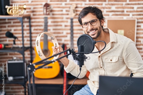 Fotografie, Obraz Young hispanic man musician singing song playing tambourine at music studio