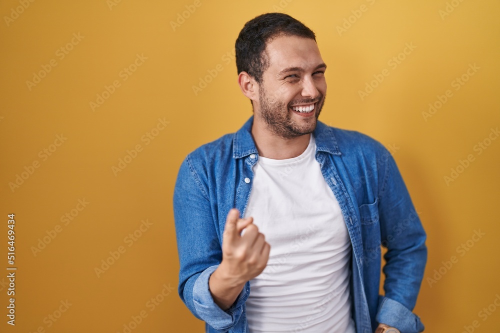 Hispanic man standing over yellow background beckoning come here gesture with hand inviting welcoming happy and smiling Hispanic man standing over yellow background beckoning come here gesture with hand inviting welcoming happy and smiling
