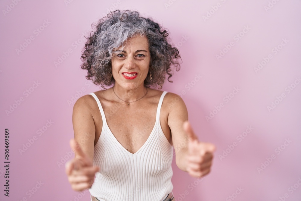 Middle age woman with grey hair standing over pink background pointing fingers to camera with happy and funny face. good energy and vibes. Middle age woman with grey hair standing over pink background pointing fingers to camera with happy and funny face. good energy and vibes.