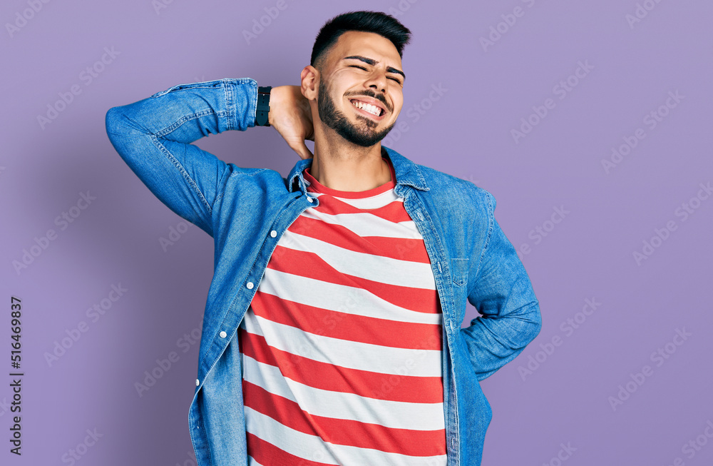 Young hispanic man with beard wearing casual denim jacket suffering of neck ache injury, touching neck with hand, muscular pain Young hispanic man with beard wearing casual denim jacket suffering of neck ache injury, touching neck with hand, muscular pain