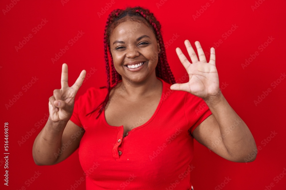 African american woman with braided hair standing over red background showing and pointing up with fingers number seven while smiling confident and happy. African american woman with braided hair standing over red background showing and pointing up with fingers number seven while smiling confident and happy.