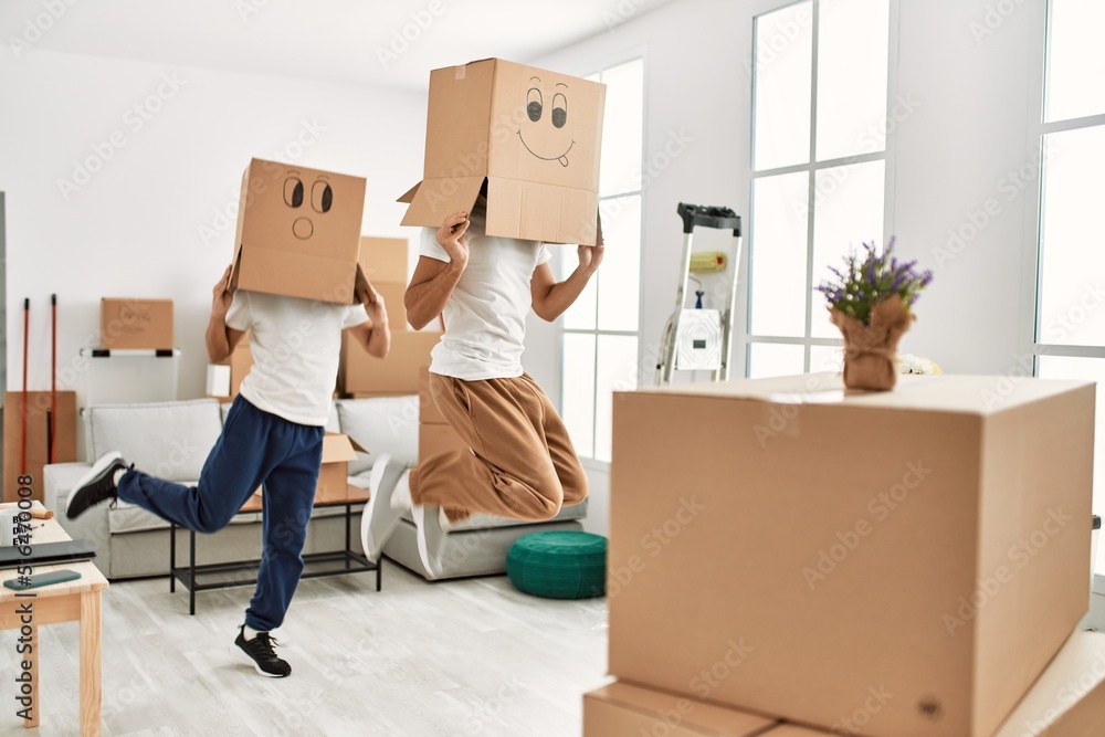 Two hispanic men couple playing with funny cardboard boxes on head at new home Two hispanic men couple playing with funny cardboard boxes on head at new home