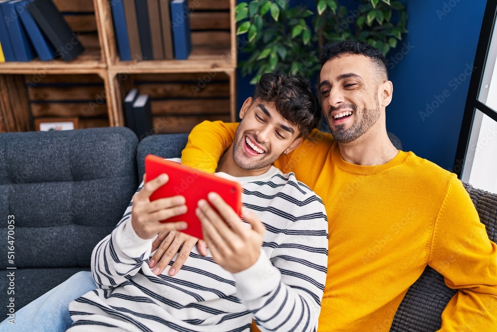 Two man couple using touchpad sitting on sofa at home