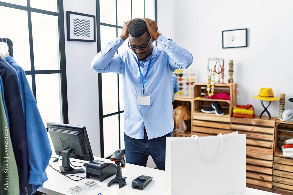 Young african man working as manager at retail boutique suffering from headache desperate and stressed because pain and migraine. hands on head. Young african man working as manager at retail boutique suffering from headache desperate and stressed because pain and migraine. hands on head.