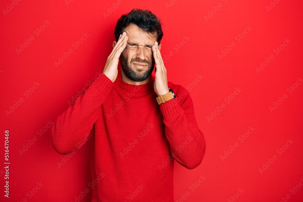 Handsome man with beard wearing casual red sweater with hand on head, headache because stress. suffering migraine. Handsome man with beard wearing casual red sweater with hand on head, headache because stress. suffering migraine.