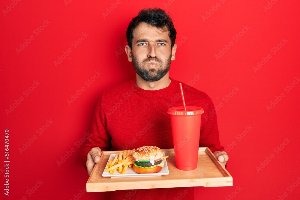 Handsome man with beard eating a tasty classic burger with fries and soda puffing cheeks with funny face. mouth inflated with air, catching air. Handsome man with beard eating a tasty classic burger with fries and soda puffing cheeks with funny face. mouth inflated with air, catching air.