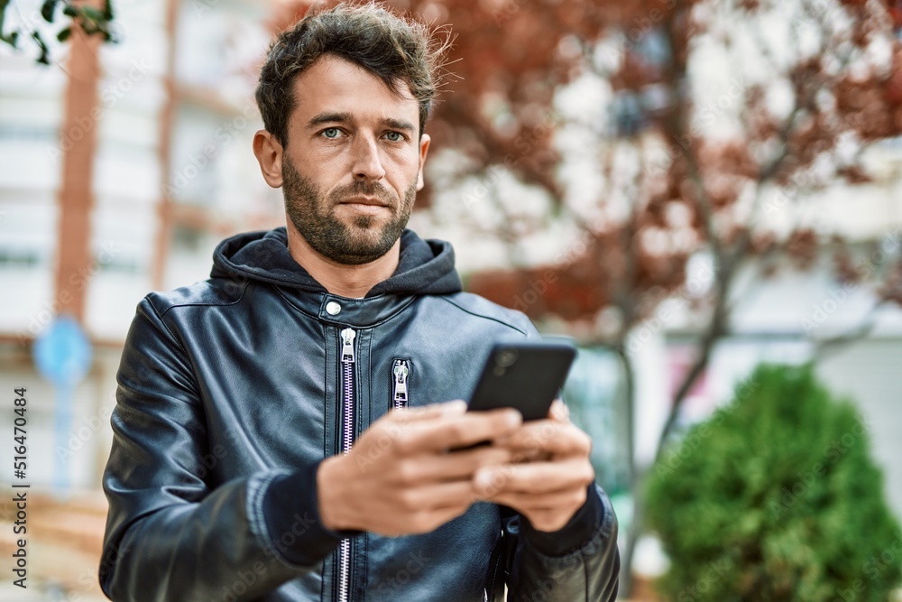 Handsome hispanic man with beard with serious face outdoors using smartphone