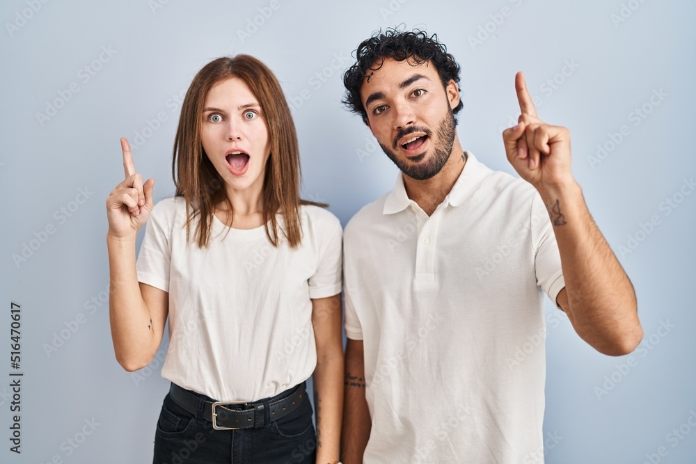 Young couple wearing casual clothes standing together pointing finger up with successful idea. exited and happy. number one. Young couple wearing casual clothes standing together pointing finger up with successful idea. exited and happy. number one.
