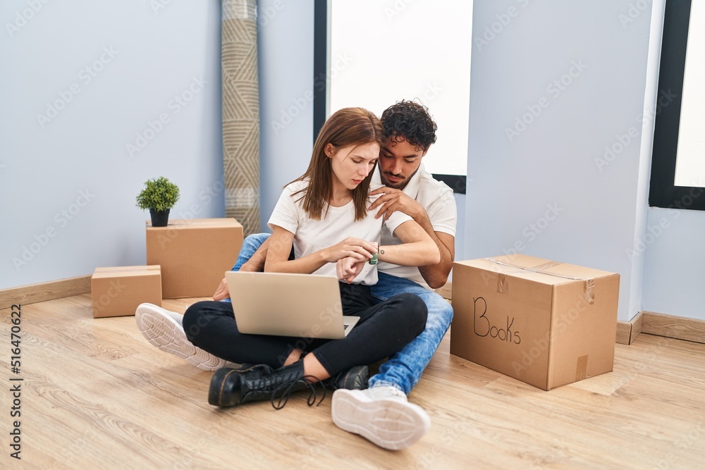 Young couple using laptop at new home checking the time on wrist watch, relaxed and confident Young couple using laptop at new home checking the time on wrist watch, relaxed and confident