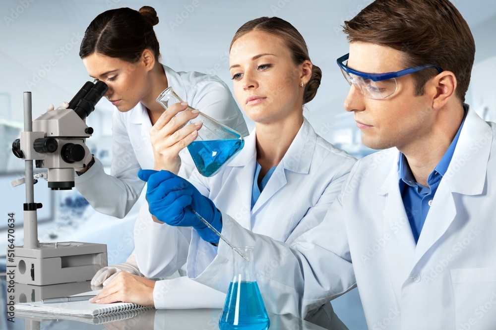 Young scientists conducting research investigations in a medical laboratory, a researcher in the foreground is using a microscope concept Young scientists conducting research investigations in a medical laboratory, a researcher in the foreground is using a microscope concept