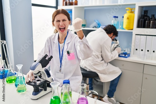 Young two people working at scientist laboratory annoyed and frustrated shouting with anger, yelling crazy with anger and hand raised