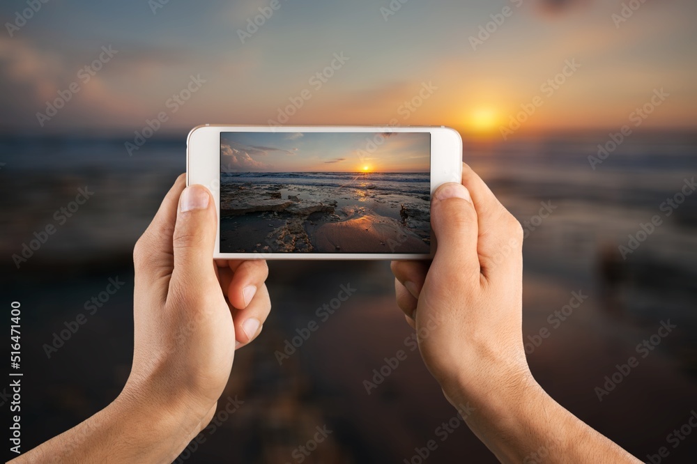 Woman holding mobile phone in hands and taking beautiful sunrise photo