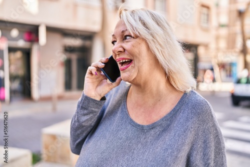 Middle age blonde woman smiling confident talking on the smartphone at street