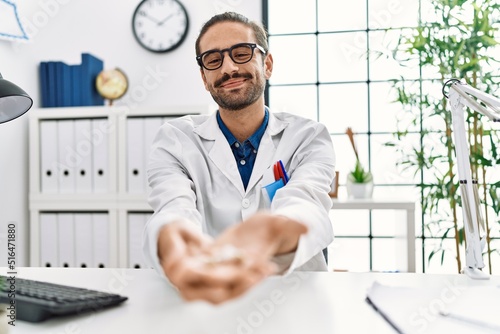 Handsome hispanic man working as audiologist holding hearing aid at hospital clinic photo