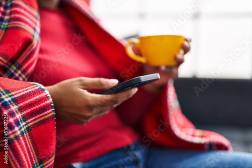 African american woman drinking coffee and using smartphone at home