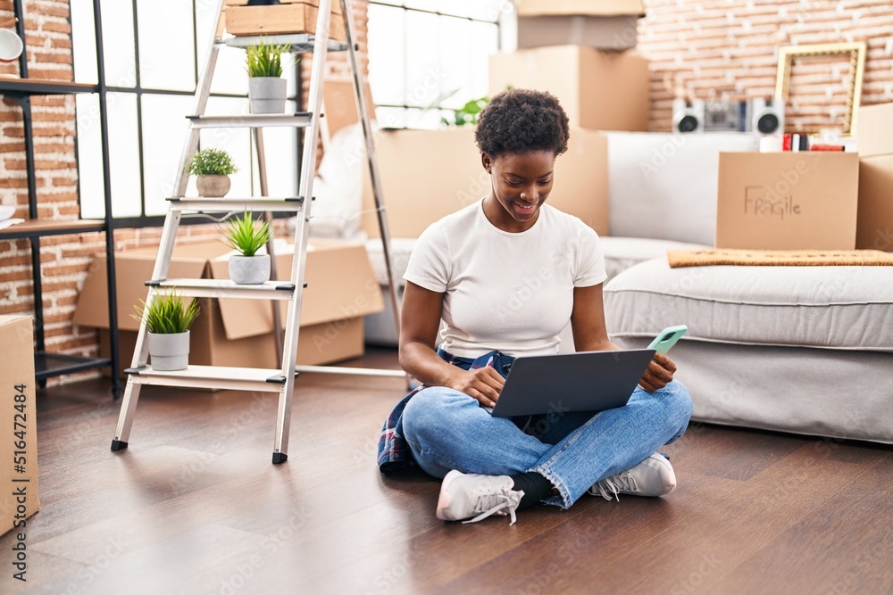 African american woman using laptop and smartphone sitting on floor at new home African american woman using laptop and smartphone sitting on floor at new home