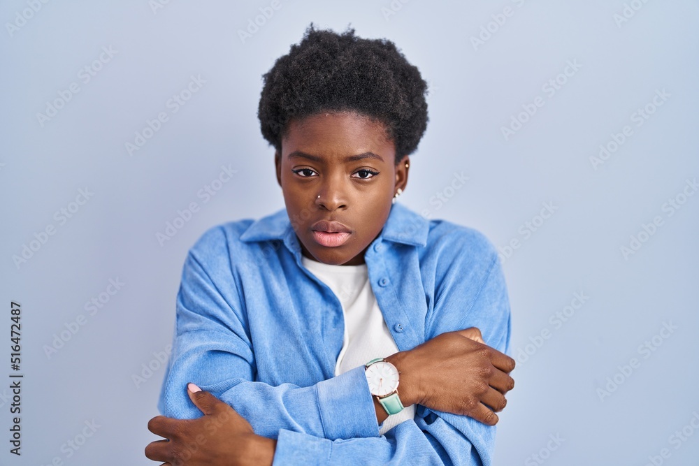 African american woman standing over blue background shaking and freezing for winter cold with sad and shock expression on face African american woman standing over blue background shaking and freezing for winter cold with sad and shock expression on face