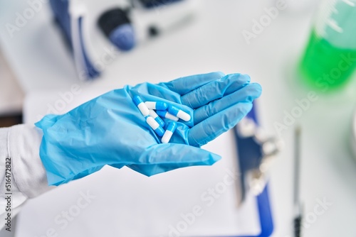 African american woman wearing gloves holding pills laboratory