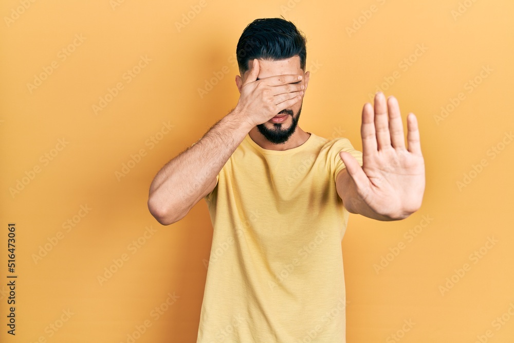 Handsome man with beard wearing casual yellow t shirt covering eyes with hands and doing stop gesture with sad and fear expression. embarrassed and negative concept. Handsome man with beard wearing casual yellow t shirt covering eyes with hands and doing stop gesture with sad and fear expression. embarrassed and negative concept.