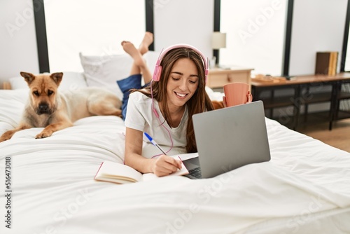 Photography Young hispanic woman studying lying on bed with dogs at bedroom
