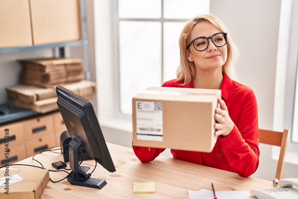 Blonde woman working at small business ecommerce holding box smiling looking to the side and staring away thinking. Blonde woman working at small business ecommerce holding box smiling looking to the side and staring away thinking.